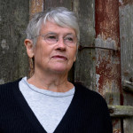 Poeten Ingela Strandbrerg framför en grå dörr.